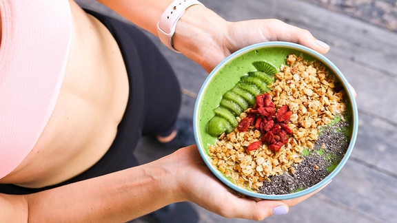 Eine Frau mit einer sportlichen Figur hält eine Bowl zum gesunden Abnehmen.